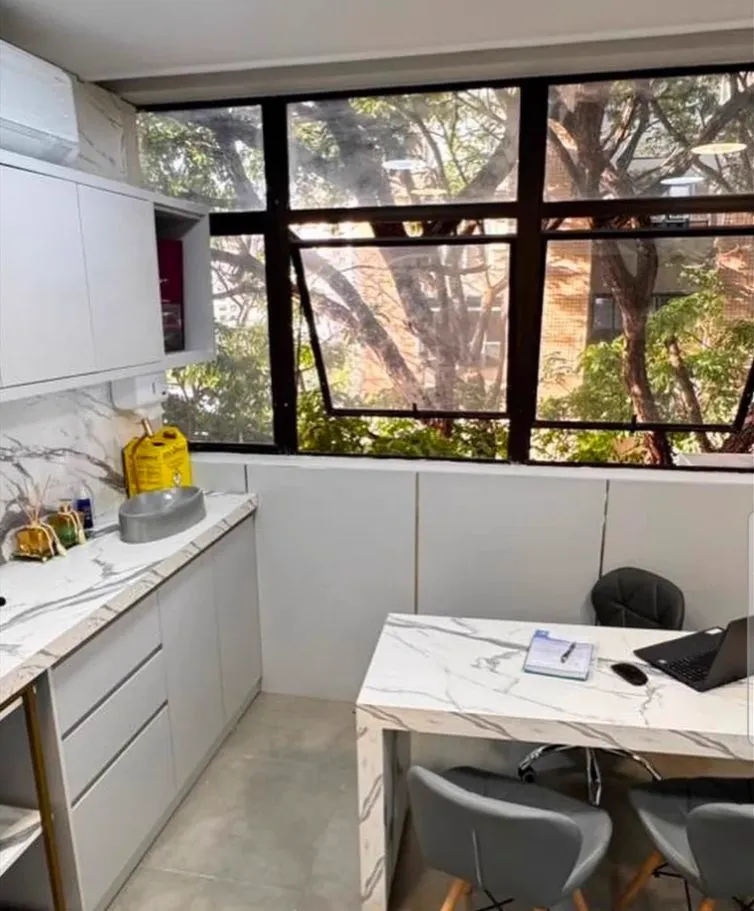 Sala de avaliação com bancada em mármore, mesa de atendimento e janela arborizada