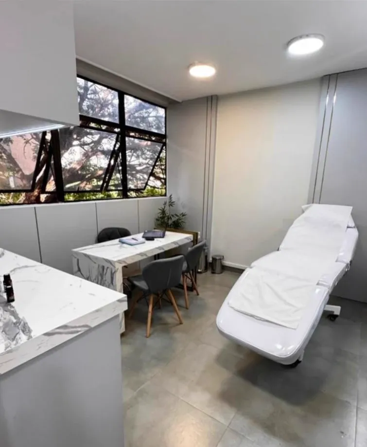 Consultório com maca, mesa de avaliação e janela com vista para as árvores
